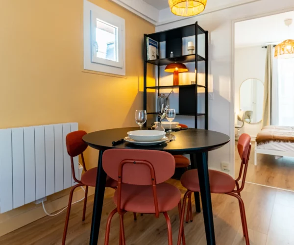 Un espace repas avec une table noire des chaises orange et un mur couleur crème entièrement rénové