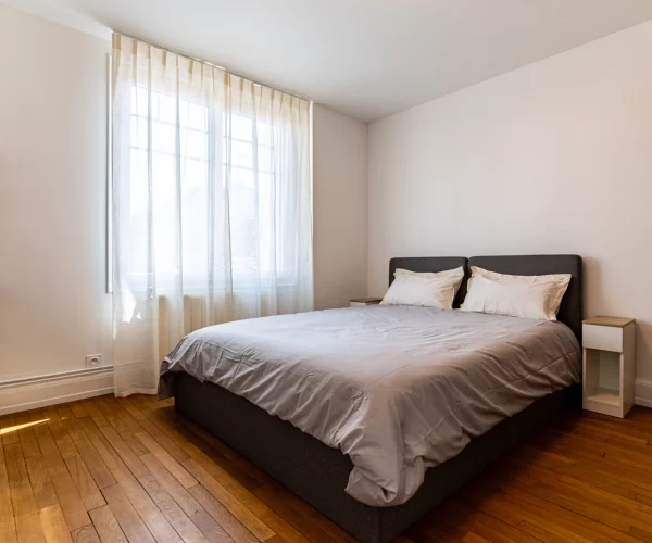 Chambre avec parquet en bois et fenêtres avec rideau